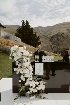 a man and woman standing in front of a bar with flowers on the table next to it