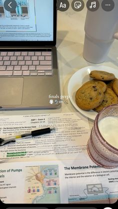 a laptop computer sitting on top of a table next to a plate of cookies and milk