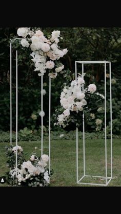 white flowers are arranged on three metal stands in the grass, with greenery behind them