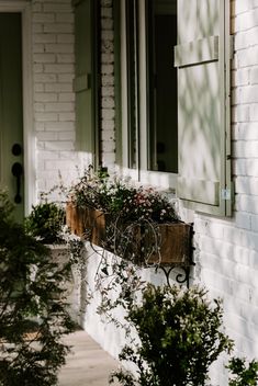 two potted plants sitting on the side of a white brick building with green shutters