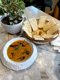 a bowl of soup and some pita bread on a table with a potted plant