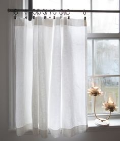 a candle is lit in front of a window with white curtains and water droplets on the windowsill