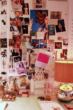 a cluttered desk with many pictures and photos on the wall next to a lamp