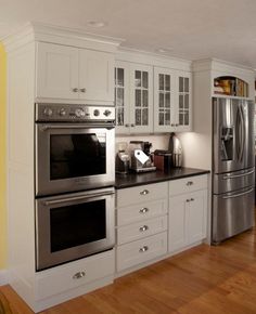 a kitchen with white cabinets and stainless steel appliances in the center, along with hardwood flooring