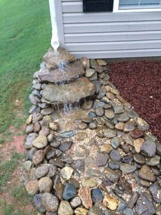 a water feature in front of a house with rocks on the ground and grass around it