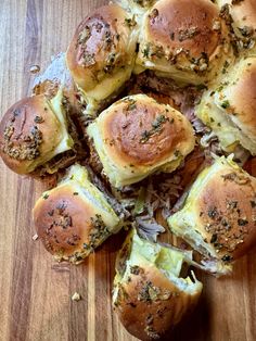 a bunch of rolls that are sitting on a wooden table with cheese and herbs all over them