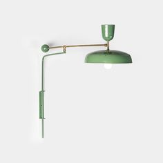 a green wall lamp on a white wall next to a light fixture with an arm