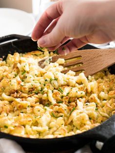 a skillet full of macaroni and cheese being stirred with a wooden spoon