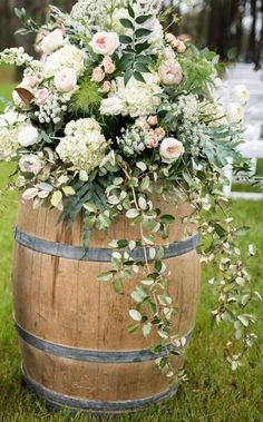 a wooden barrel with flowers and greenery in it sitting on the grass next to an aisle