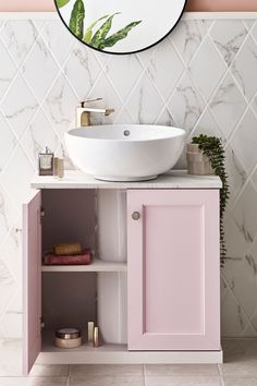 a white sink sitting under a round mirror next to a pink cabinet and counter top