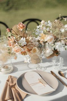 the table is set with white and peach flowers in vases, silverware, and napkins