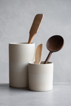 three wooden spoons and two white cups on a gray surface with grey wall in the background