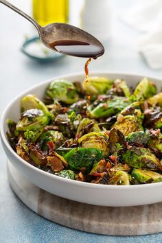 brussel sprouts in a white bowl being drizzled with dressing