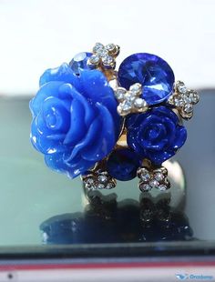 a blue rose and diamond ring sitting on top of a glass table next to a cell phone