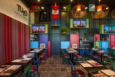 the interior of a restaurant with colorful tables and chairs, televisions on the wall