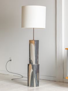 a lamp that is sitting on the floor next to a wall with a painting on it