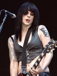 a woman with black hair and piercings playing an electric guitar