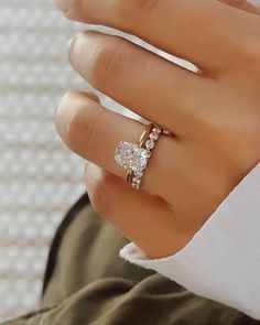 a woman's hand with a diamond ring on her left hand and the other hand holding an engagement ring