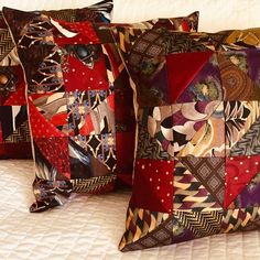 two decorative pillows sitting on top of a white bed covered in red and brown fabric