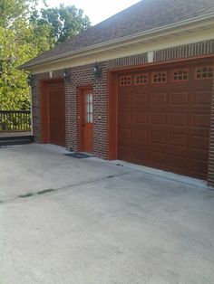 two brown garage doors are open in front of a brick building with a black fence