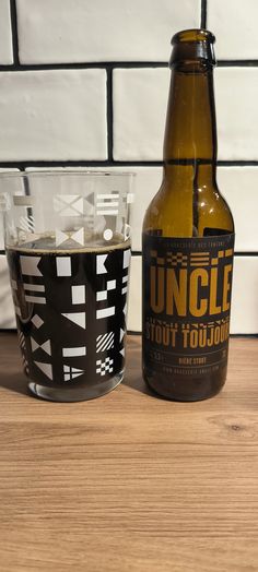 a beer bottle next to a shot glass on a wooden table with white tiles in the background