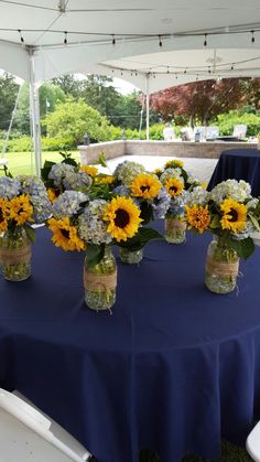 sunflowers and hydrangeas are arranged in mason jars on a blue tablecloth