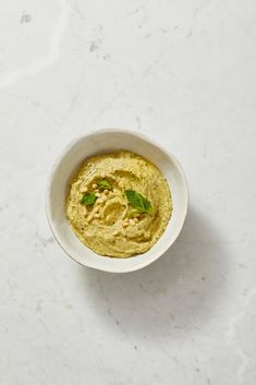 a white bowl filled with hummus and garnished with mint leaves on top