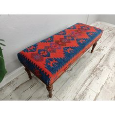 a bench with an orange, blue and red design on the seat is next to a potted plant