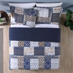 a bed covered in blue and white quilts next to a night stand with an alarm clock