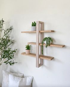 three wooden shelves with plants on them against a white wall next to a couch and potted plant