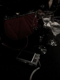 two wine glasses sitting on top of a table next to a cell phone and purse