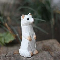 a white cat figurine sitting on top of a wooden table next to a plant