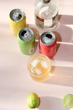 three cans of soda and two limes on a white table with shadows from the top