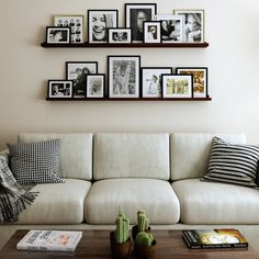 a white couch sitting next to a wooden coffee table in front of a wall filled with pictures