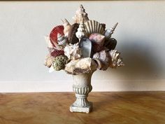 a vase filled with seashells sitting on top of a wooden table next to a wall