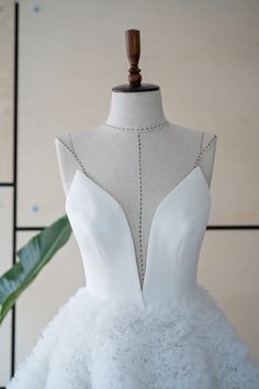 the back of a white wedding dress on a mannequin with a green plant behind it