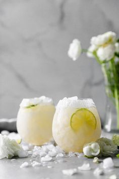 two margaritas with lime slices and white flowers in the background on a countertop