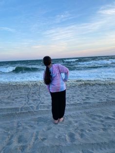 a woman standing on top of a sandy beach next to the ocean