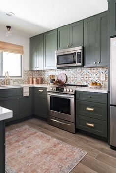 a kitchen with green cabinets, silver appliances and an area rug on the floor in front of the stove