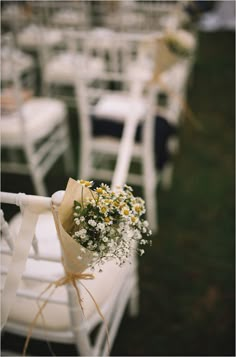 a bunch of white chairs with flowers tied to them