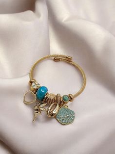 This steel bracelet is adorned with elegant details featuring seashells, pearls, a mermaid, and other sea-themed charms. The combination of turquoise and white tones adds a touch of elegance and a striking look to the bracelet. Perfect for summer and beach-themed outfits, this bracelet also makes a thoughtful gift for your loved ones. With its unique design and high-quality materials, this stylish bracelet is a lasting accessory that will complement your style. Features: Material: Steel, pearl, Metal Charm Bracelets For Beach, Adjustable Gold Charm Bracelet Ocean-inspired, Beach Metal Bracelets With Charms, Turquoise Metal Charm Bracelet As Gift, Turquoise Metal Charm Bracelet Gift, Pandora Bracelet Designs, Bracelet Pandora, Whimsical Jewelry, Bracelets Design