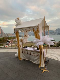 a canopy bed decorated with white feathers and gold trimmings in front of the water