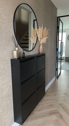 a black dresser sitting in front of a mirror on top of a wooden floor next to a wall