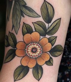 an orange flower with green leaves on it's side tattoo by the artist in progress