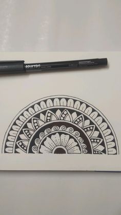 a pen sitting on top of a piece of paper next to a drawing pad with an intricate design