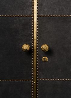 two golden knobs on the side of a black door with gold studs and rivets