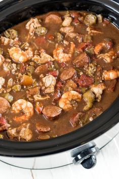 a crock pot filled with meat and vegetables on top of a white countertop