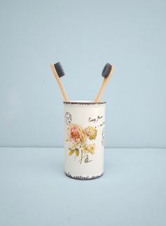 two toothbrushes in a cup with flowers on the inside and writing on the outside