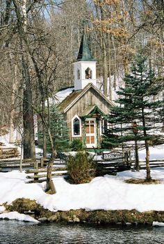 a small church with a steeple surrounded by trees in the wintertime, and snow on the ground