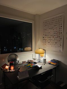 a desk with a lamp, books and other items on it in front of a window